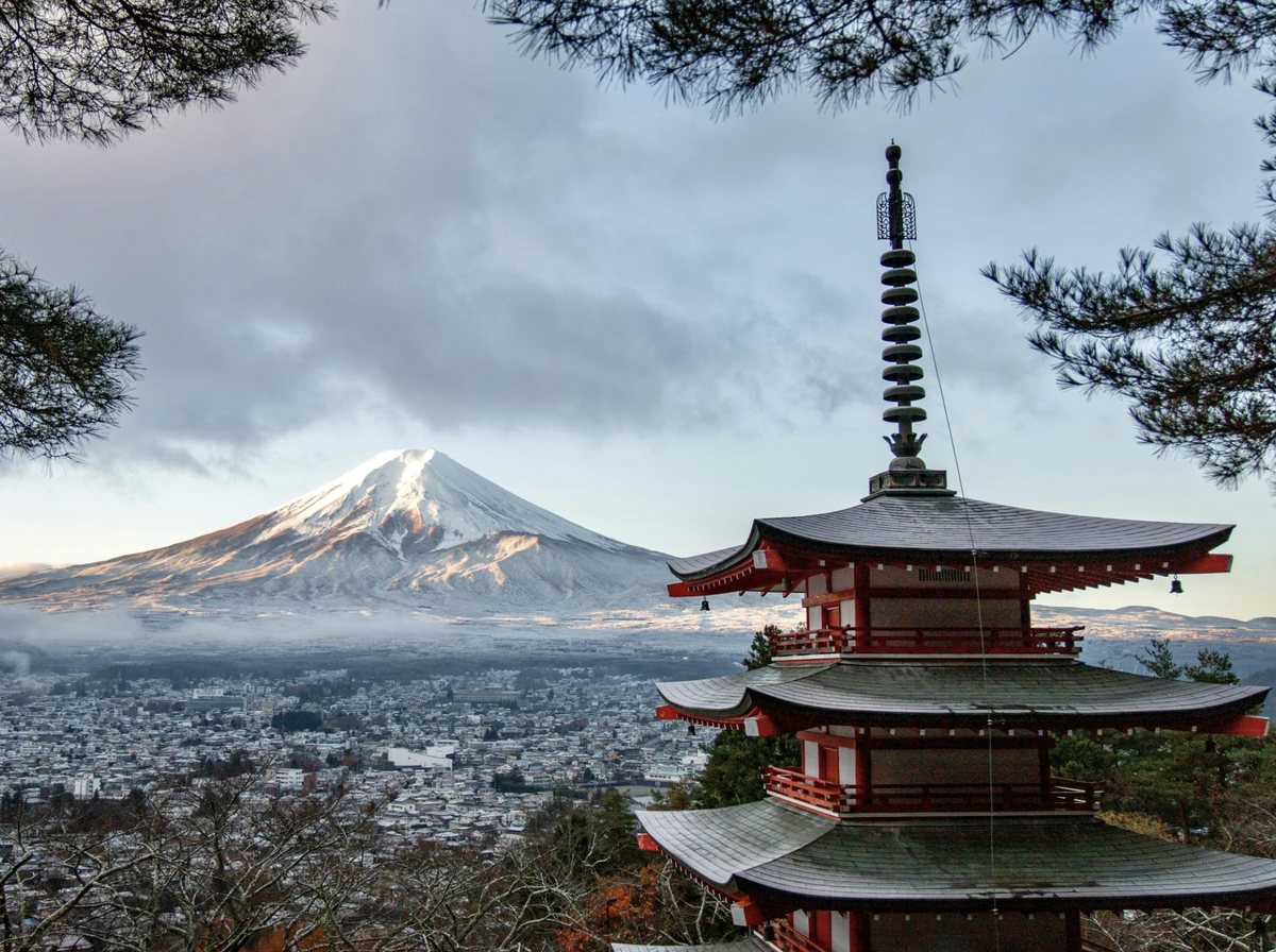 Mount Fuji rising beyond a red pagoda and pine branches in Japan
